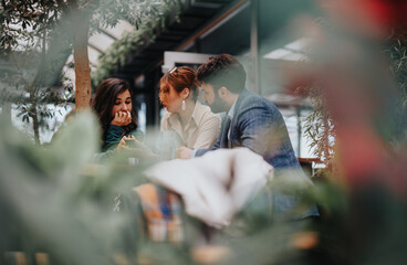 Three entrepreneurs engaged in a serious business discussion at a cozy urban cafe, planning their...