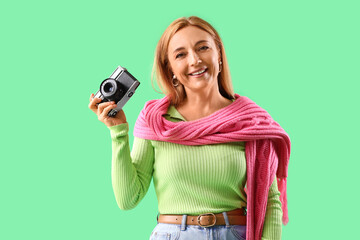 Stylish mature woman with photo camera on green background