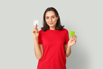 Young woman with condoms on grey background. Safe sex concept