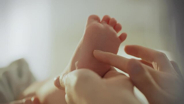 Showing attentiveness and care close-up of a mother's hands gently stroking the legs of her newborn baby's feet, giving a massage to train sensitivity