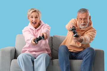 Mature couple playing video game on sofa against blue background