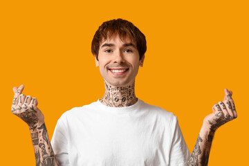 Handsome young man making hearts with fingers on yellow background