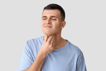 Young man suffering from sore throat on light background, closeup
