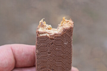 one brown broken chocolate bar with nougat and peanuts lies in the palm of his hand on a gray...
