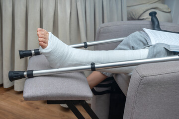 Person with broken leg in a plaster cast with crutches at home. Health care insurance.