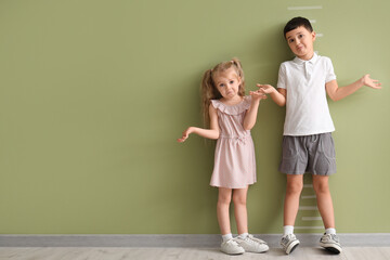 Confused little kids measuring height near green wall