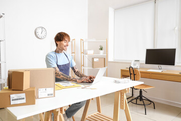 Young online store seller working with laptop at table in warehouse