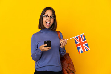 Young latin woman holding an United Kingdom flag isolated on yellow background surprised and...
