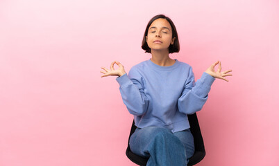 Young mixed race woman sitting on a chair isolated on pink background in zen pose