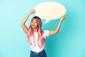 Young mixed race woman with pink hair isolated on blue background holding an empty speech bubble