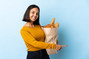 Young latin woman buying some breads isolated on blue background pointing finger to the side and...