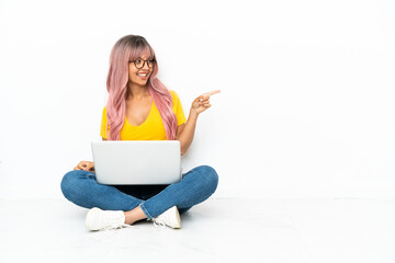 Young mixed race woman with a laptop with pink hair sitting on the floor isolated on white...