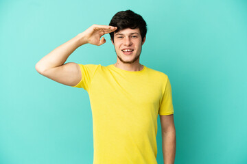 Young Russian man isolated on blue background saluting with hand with happy expression