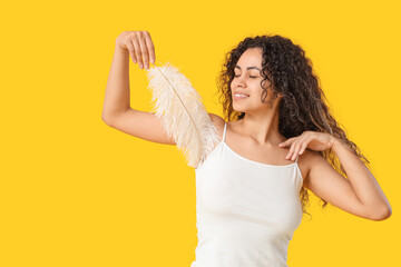 Beautiful young happy woman with feather on yellow background. Depilation concept