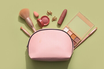 Cosmetic bag with makeup products, brushes and earrings on green background
