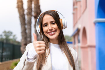 Young pretty woman at outdoors listening music and with thumb up