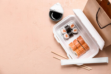 Plastic container with tasty sushi rolls, chopsticks and paper bag on beige grunge background....