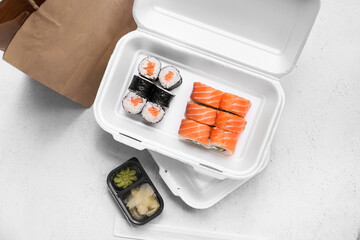 Plastic containers with tasty sushi rolls, marinated ginger and paper bag on white grunge background. Delivery concept