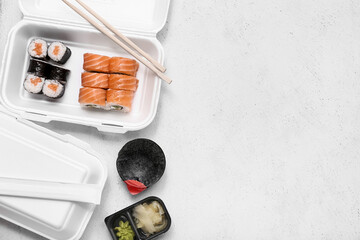 Plastic containers with tasty sushi rolls, soy sauce and chopsticks on white grunge background. Delivery concept