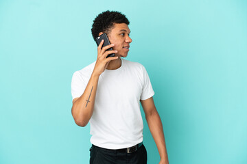 Young African American man isolated on blue background keeping a conversation with the mobile phone...