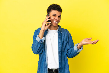 Young African American man isolated on yellow background keeping a conversation with the mobile...