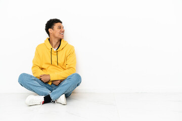 Young African American man sitting on the floor isolated on white background laughing in lateral...