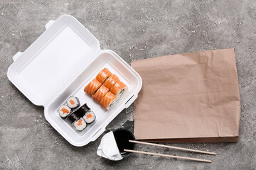 Plastic container with tasty sushi rolls, soy sauce and paper bag on grey grunge background....