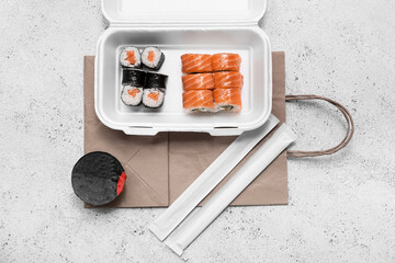 Plastic container with tasty sushi rolls, chopsticks and paper bag on white grunge background....