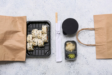 Plastic plate with tasty sushi rolls, chopsticks and paper bags on light grunge background. Delivery concept