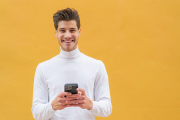 Young caucasian man at outdoors looking at the camera and smiling while using the mobile