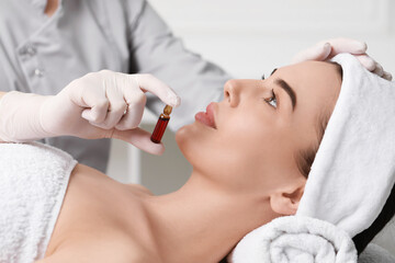 Professional cosmetologist holding skincare ampoule while working with client in clinic, closeup