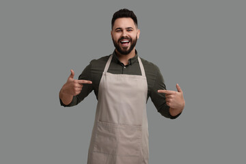 Happy man pointing at kitchen apron on grey background. Mockup for design