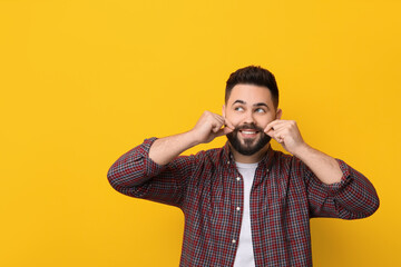 Happy young man touching mustache on yellow background. Space for text