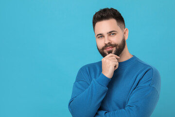 Young man with mustache touching face on light blue background. Space for text