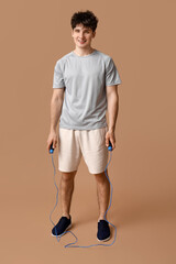 Sporty guy with jumping rope on beige background