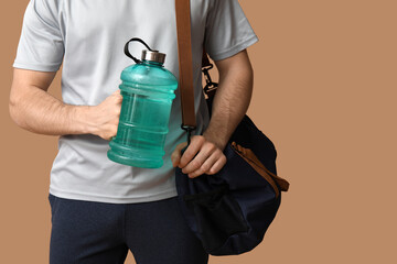 Sporty guy with bottle of water and bag on beige background, closeup