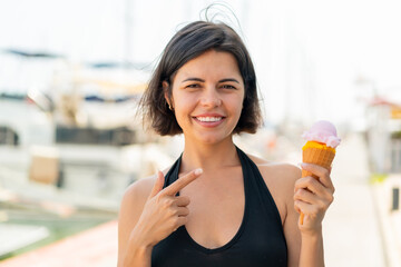 Young pretty Bulgarian woman with a cornet ice cream at outdoors and pointing it
