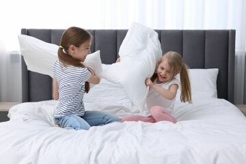 Fototapeta premium Cute little sisters having pillow fight on bed at home
