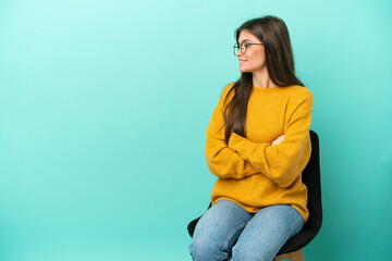 Young caucasian woman sitting on a chair isolated on blue background in lateral position