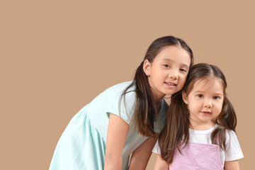 Cute little Asian happy sisters on beige background