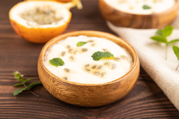 Yoghurt with granadilla and mint in wooden bowl on brown wooden, side view, selective focus.