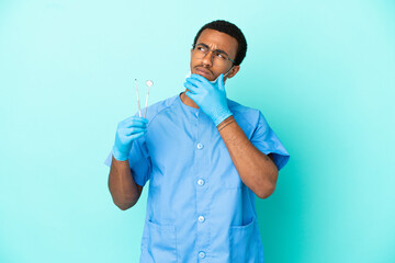 African American dentist holding tools over isolated blue background having doubts