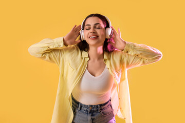 Beautiful young happy woman in headphones listening music on yellow background