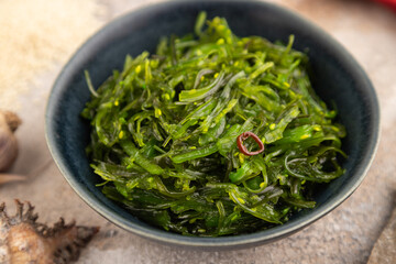 Chuka seaweed salad in blue ceramic bowl on brown concrete. Side view, selective focus