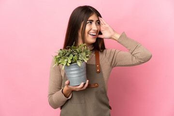 Young gardener girl holding a plant isolated on pink background smiling a lot