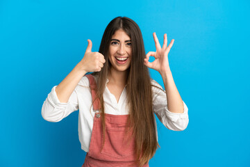 Young caucasian woman isolated on blue background showing ok sign and thumb up gesture