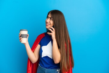 Super Hero caucasian woman isolated on blue background holding coffee to take away and a mobile