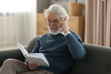 Fototapeta premium Portrait of happy grandpa reading book on sofa indoors