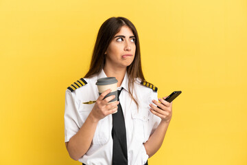 Airplane pilot isolated on yellow background holding coffee to take away and a mobile while...