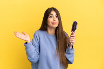 Young caucasian woman holding hairbrush isolated on blue background having doubts while raising...